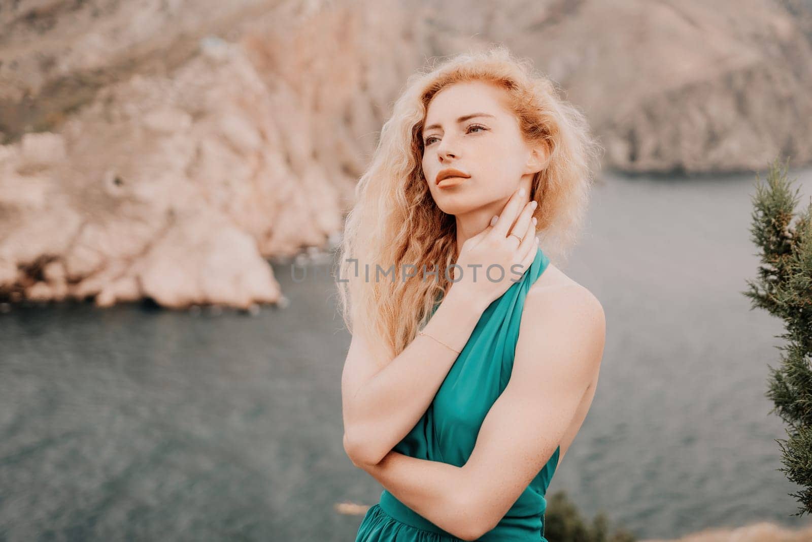 Redhead woman portrait. Curly redhead young caucasian woman with freckles looking at camera and smiling. Close up portrait cute woman in a mint long dress posing on a volcanic rock high above the sea by panophotograph