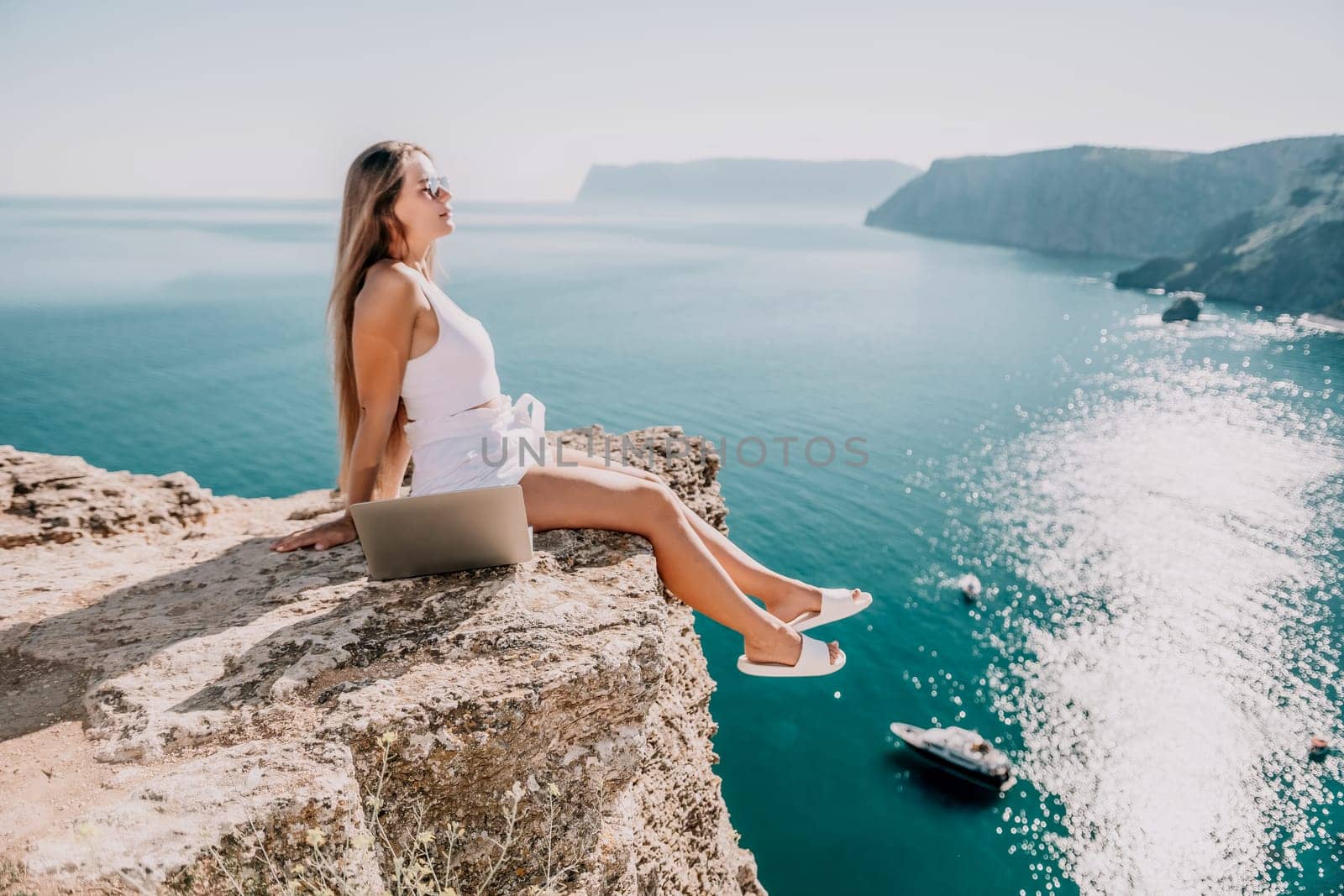 Digital nomad, Business woman working on laptop by the sea. Pretty lady typing on computer by the sea at sunset, makes a business transaction online from a distance. Freelance, remote work on vacation by panophotograph