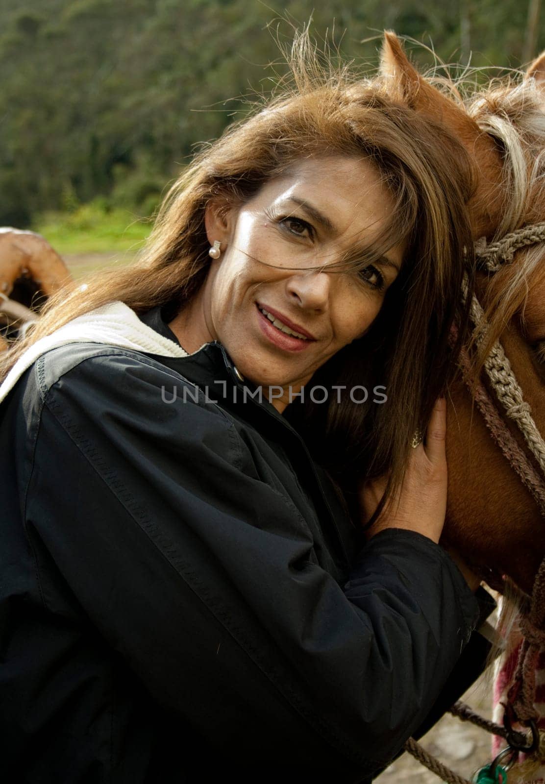 attractive lady looking at camera and hugging her horse's head. she loves horseback riding in nature