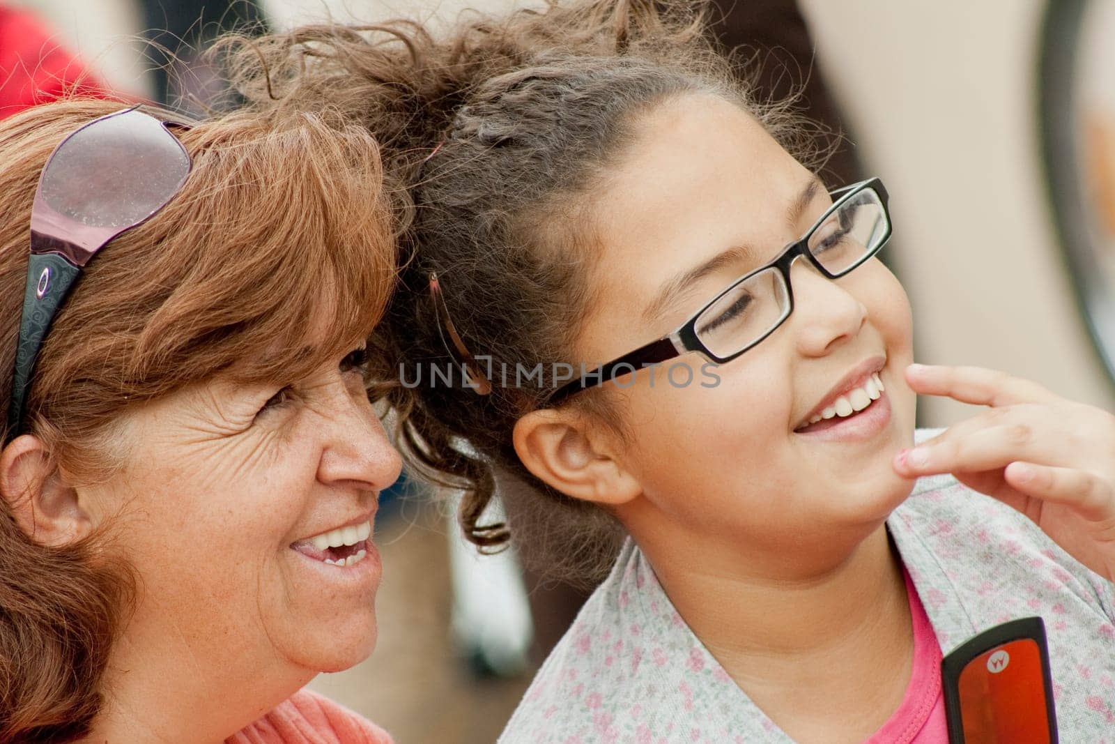 closeup of a mother and daughter in the street together smiling and looking at the same place by Raulmartin