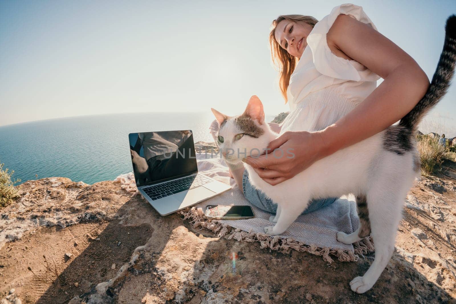 Woman sea laptop. Business woman petting cat and working on laptop by the sea. Close up on hands of pretty lady typing on computer outdoors summer day. Freelance, digital nomad and holidays concept. by panophotograph