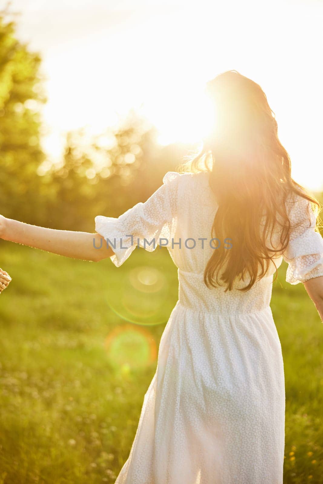 close up photo of a silhouette of a girl in a light dress standing with her back to the camera in a chamomile field during sunset. High quality photo