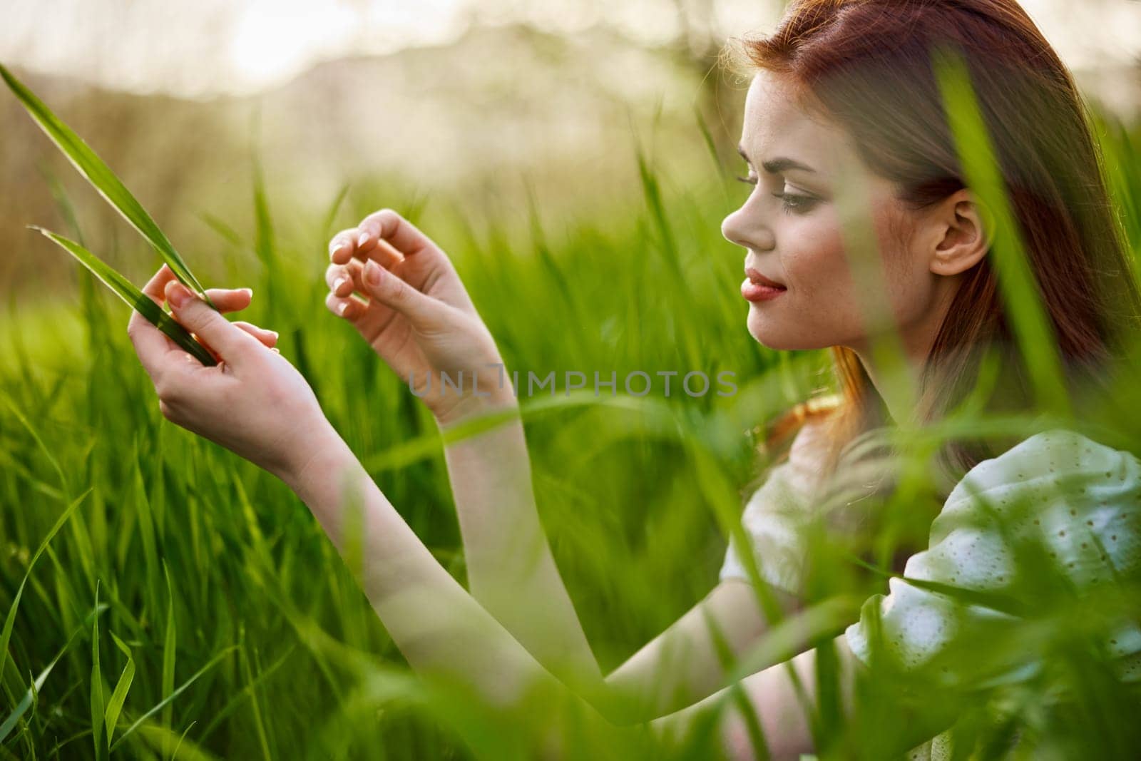 portrait of a blissfully smiling woman sitting in the grass with a leaf in her hand. High quality photo