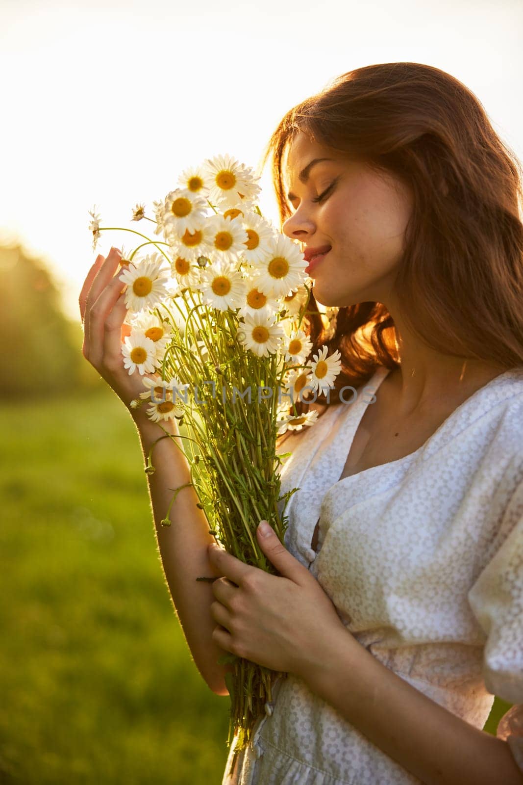 close-up portrait of a woman in a light dress in a field during sunset with a bouquet of daisies in her hands in backlight by Vichizh