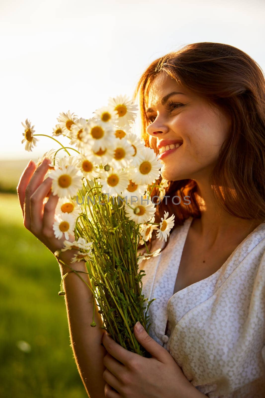 close-up portrait of a woman in a light dress in a field during sunset with a bouquet of daisies in her hands in backlight. High quality photo