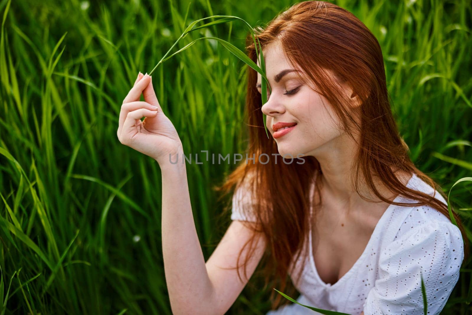 portrait of a cute red-haired woman sitting in tall grass and holding a leaf in her hands. High quality photo