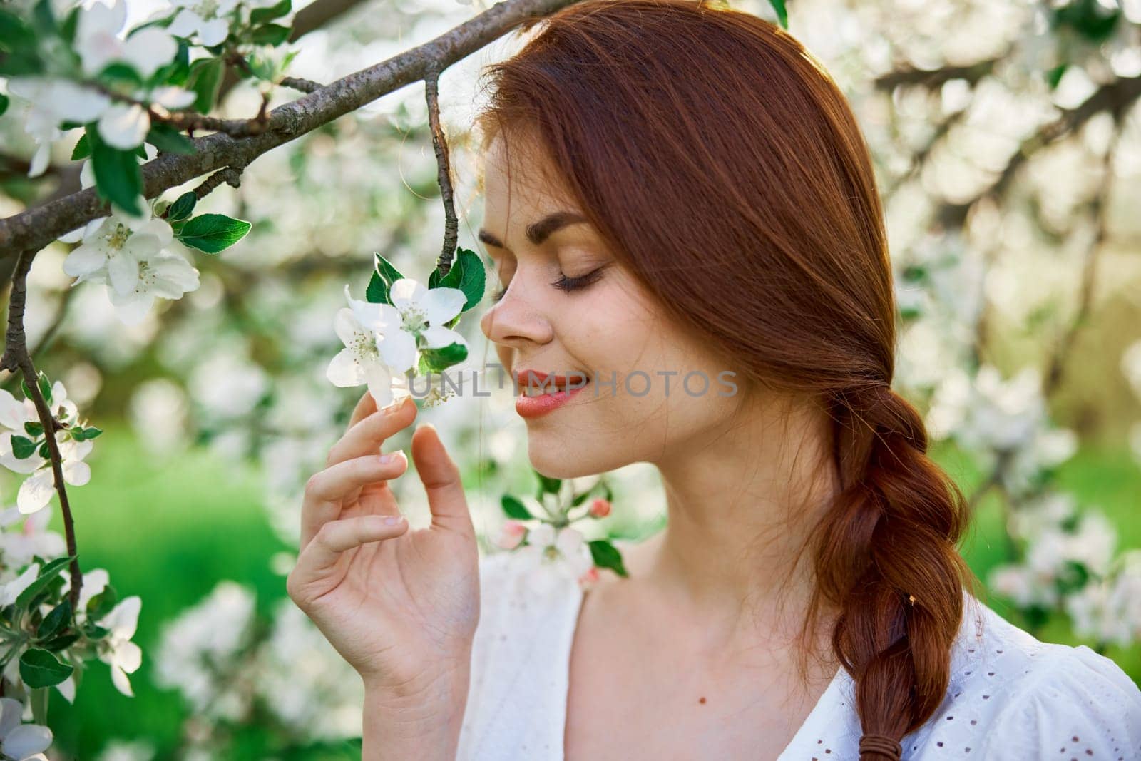 close portrait of a red-haired, laughing woman smelling flowers from a tree. High quality photo