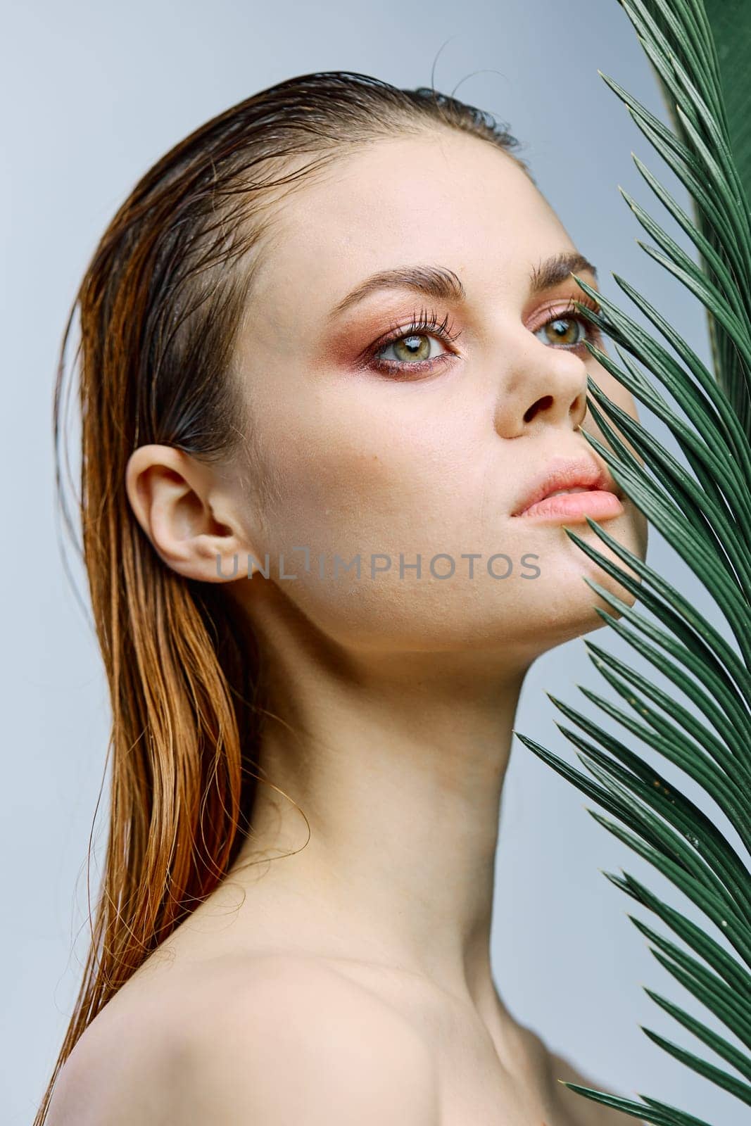 beauty portrait of a beautiful, elegant woman standing holding a palm leaf near her face, looking away. Vertical photo without retouching of problem skin by Vichizh