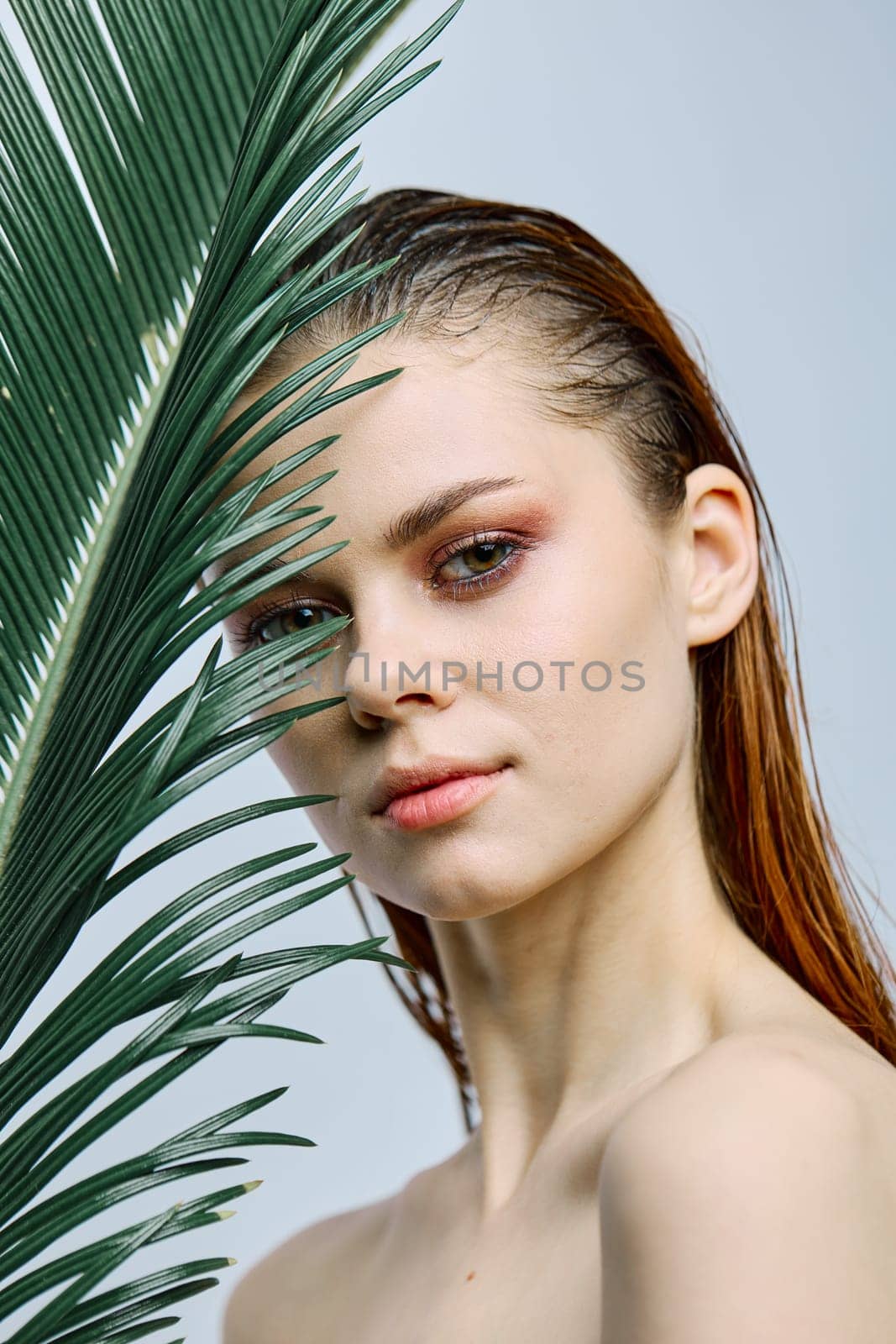 a close beauty portrait of a beautiful woman standing holding a tropical palm leaf in her hand, bringing it to her face. Vertical photo without retouching by Vichizh