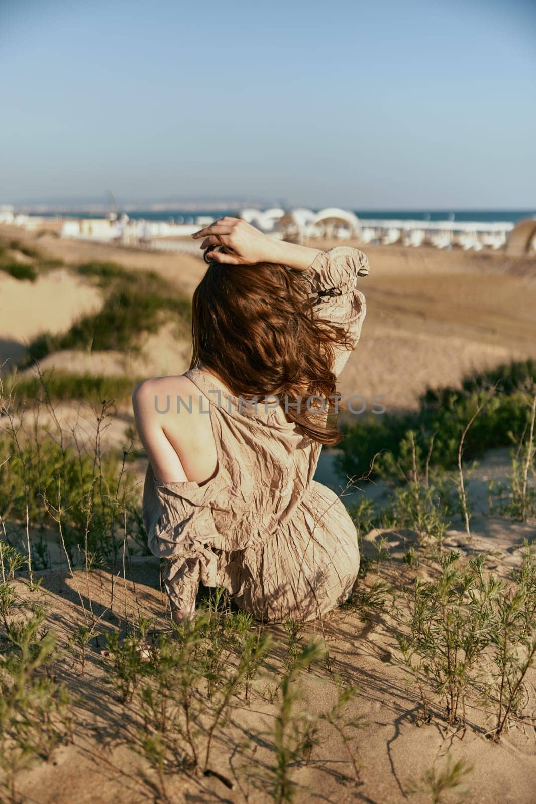 red-haired woman posing while sitting with her back to the camera holding her hair with her hand on the sea coast. High quality photo