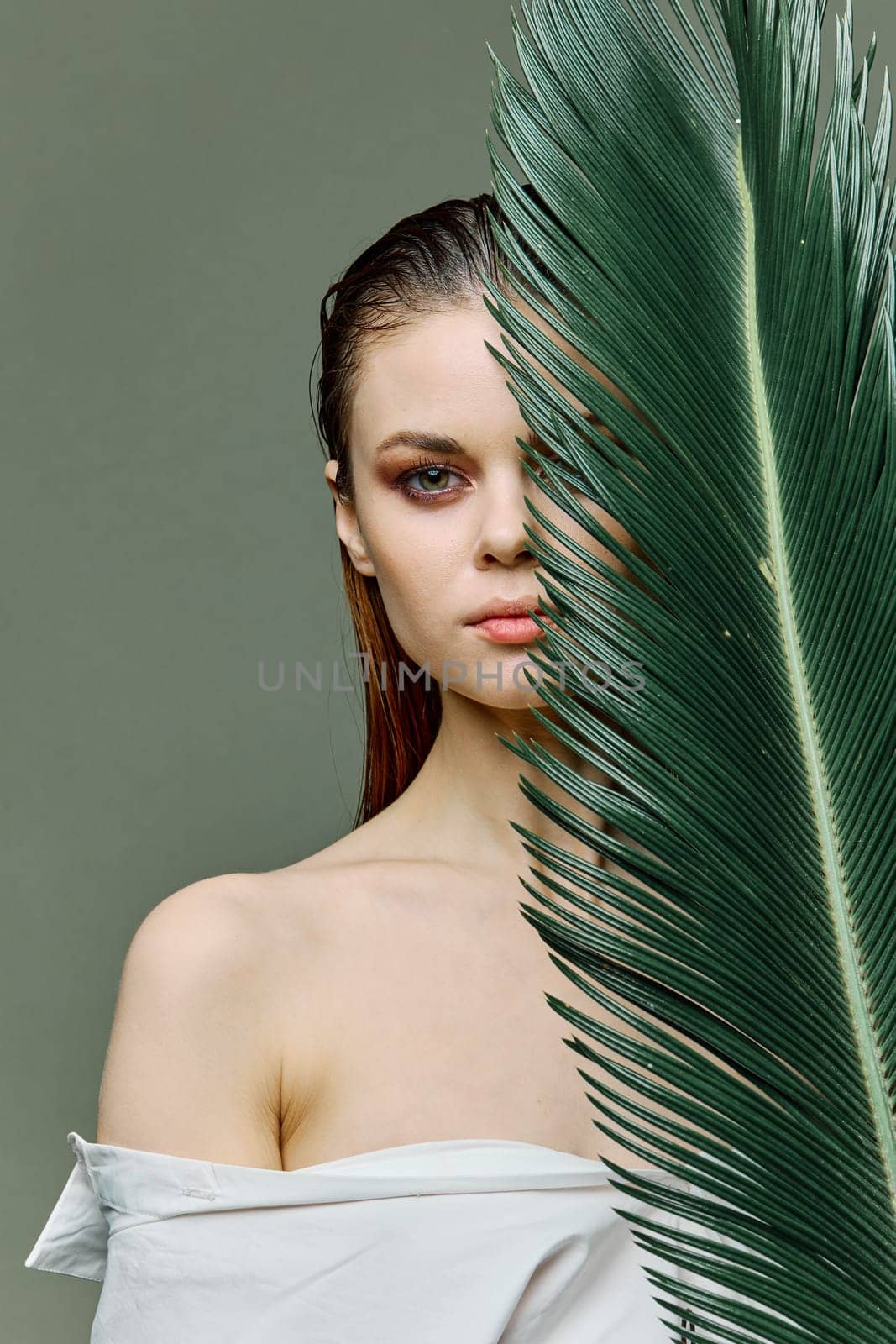 vertical photo portrait of an elegant woman with her hair slicked back, standing with a palm leaf holding it near her face by Vichizh