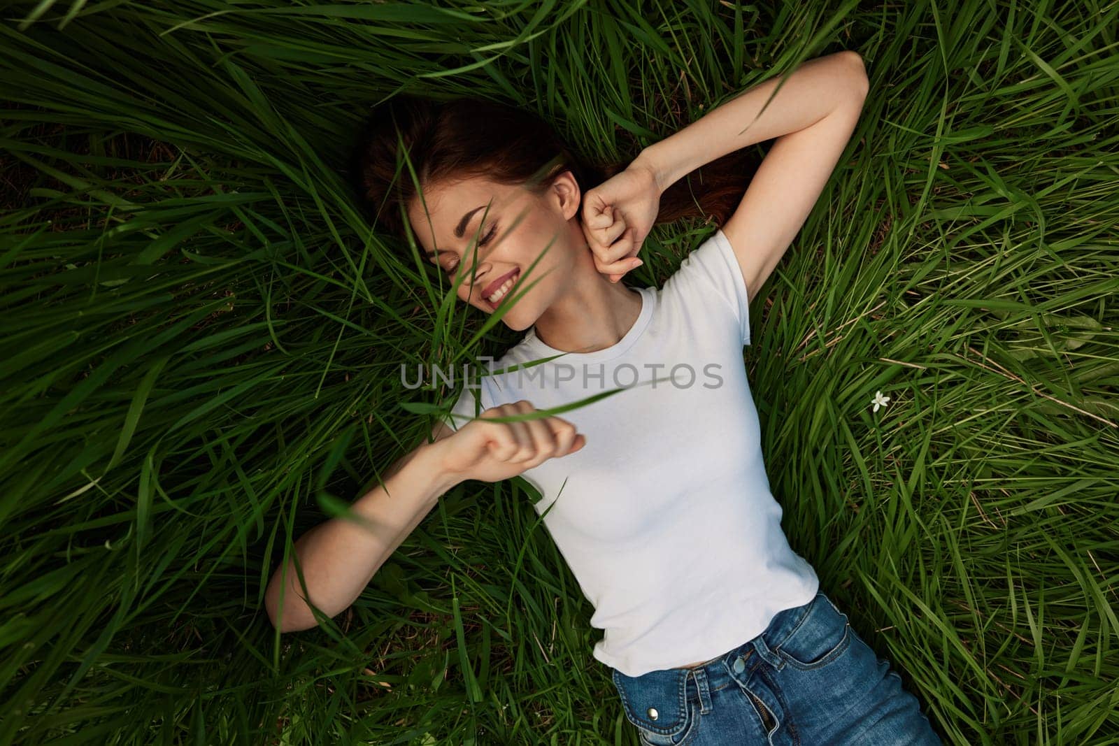 joyful, happy, carefree woman lies on the grass with her arms outstretched by Vichizh