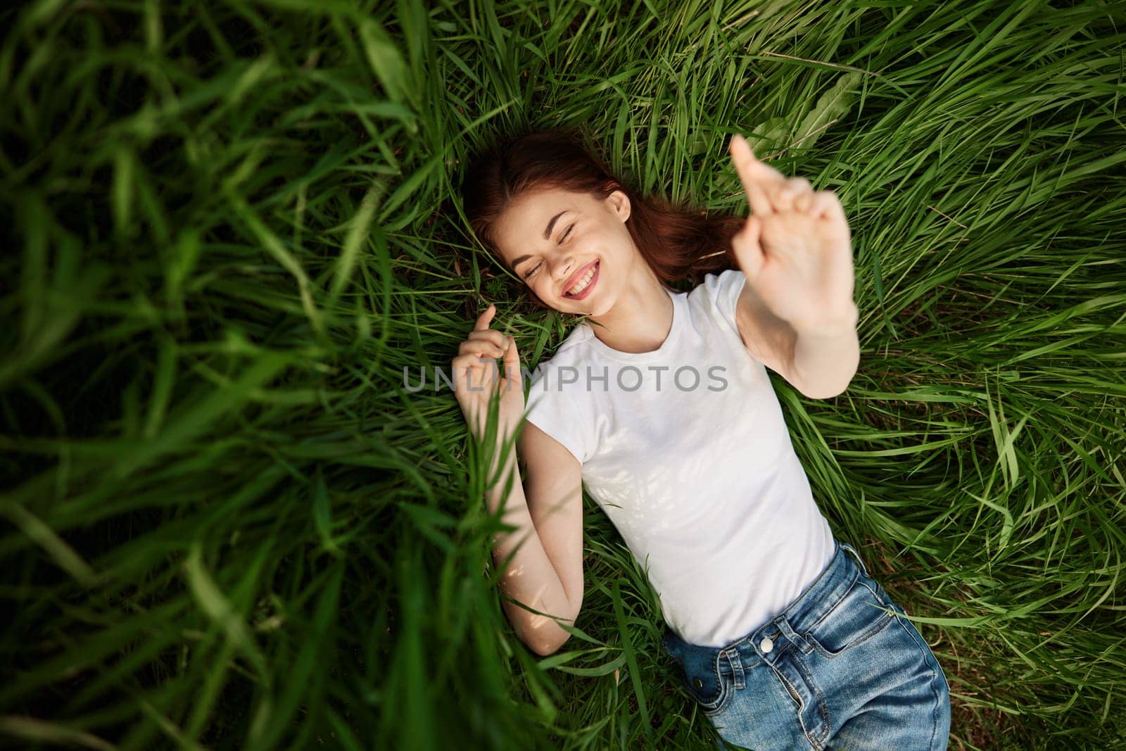 attractive teenager lying down on green grass with hands rised up to the air by Vichizh