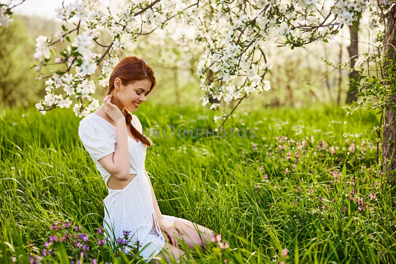 a young woman in a light summer dress is resting sitting under a flowering tree by Vichizh