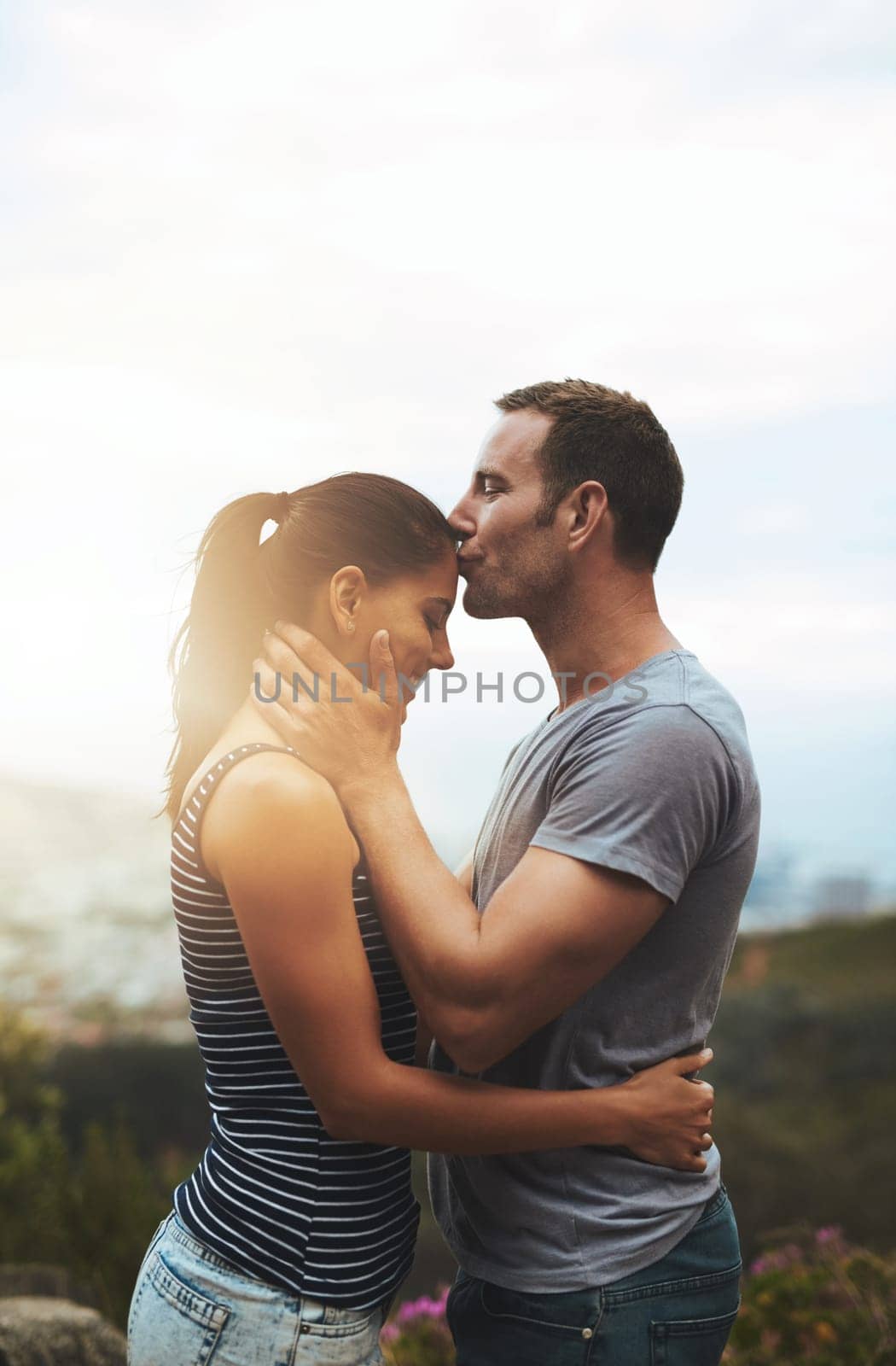 Loving to their hearts content. a young man affectionately kissing his girlfriend on her forehead outdoors. by YuriArcurs