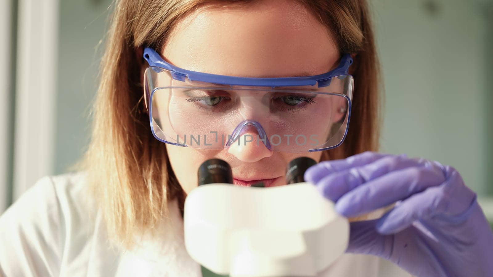 Scientist chemist in protective glasses looking through microscope in chemical laboratory by kuprevich