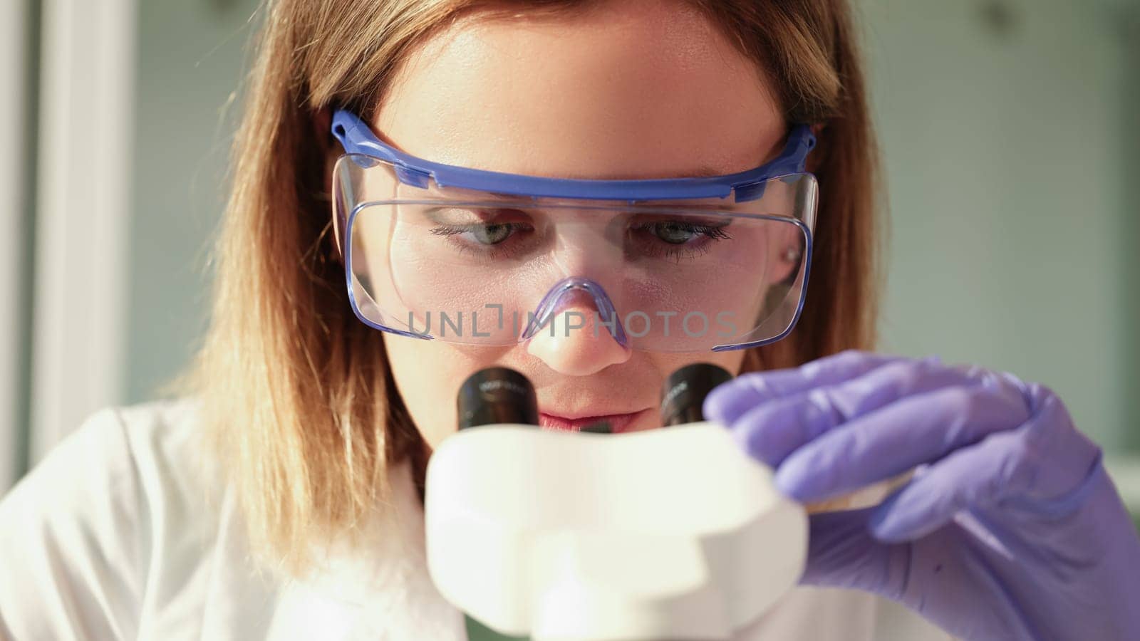 Scientist chemist in protective glasses looking through microscope in chemical lab. Laboratory medical blood tests concept