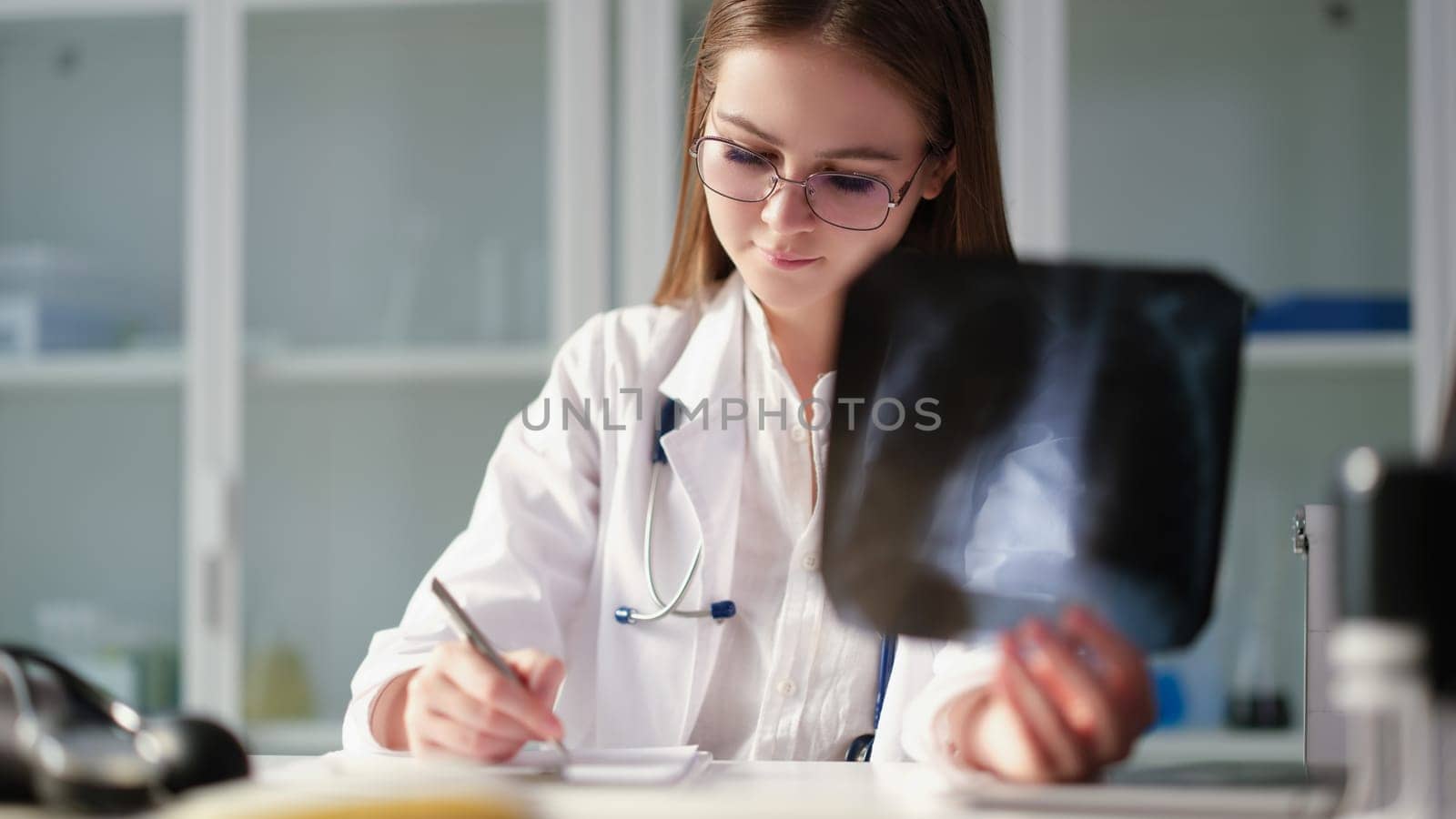 Therapist doctor holding xray of lungs in hands and writing in medical documents in clinic. Diagnosis and treatment of pneumonia and lung cancer concept