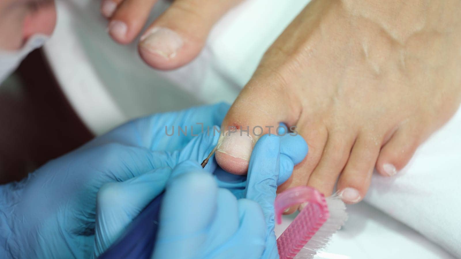 Master in gloves making pedicure on toenails in beauty salon using drill closeup. Beauty services concept