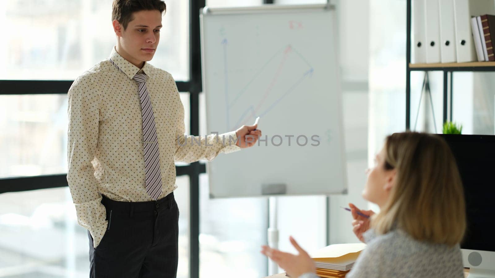 Business coach showing charts on blackboard to student in office. Business education concept