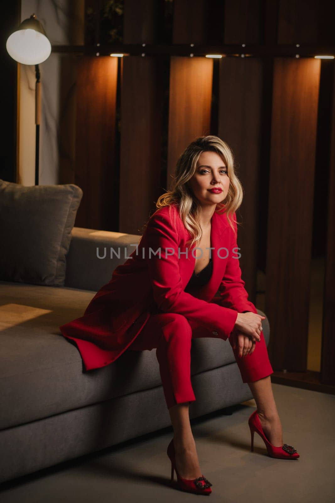 a beautiful girl dressed in a red formal suit posing in a modern interior.