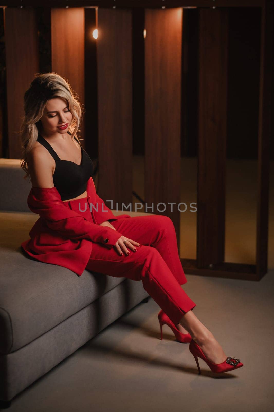 a beautiful girl dressed in a red formal suit posing in a modern interior.