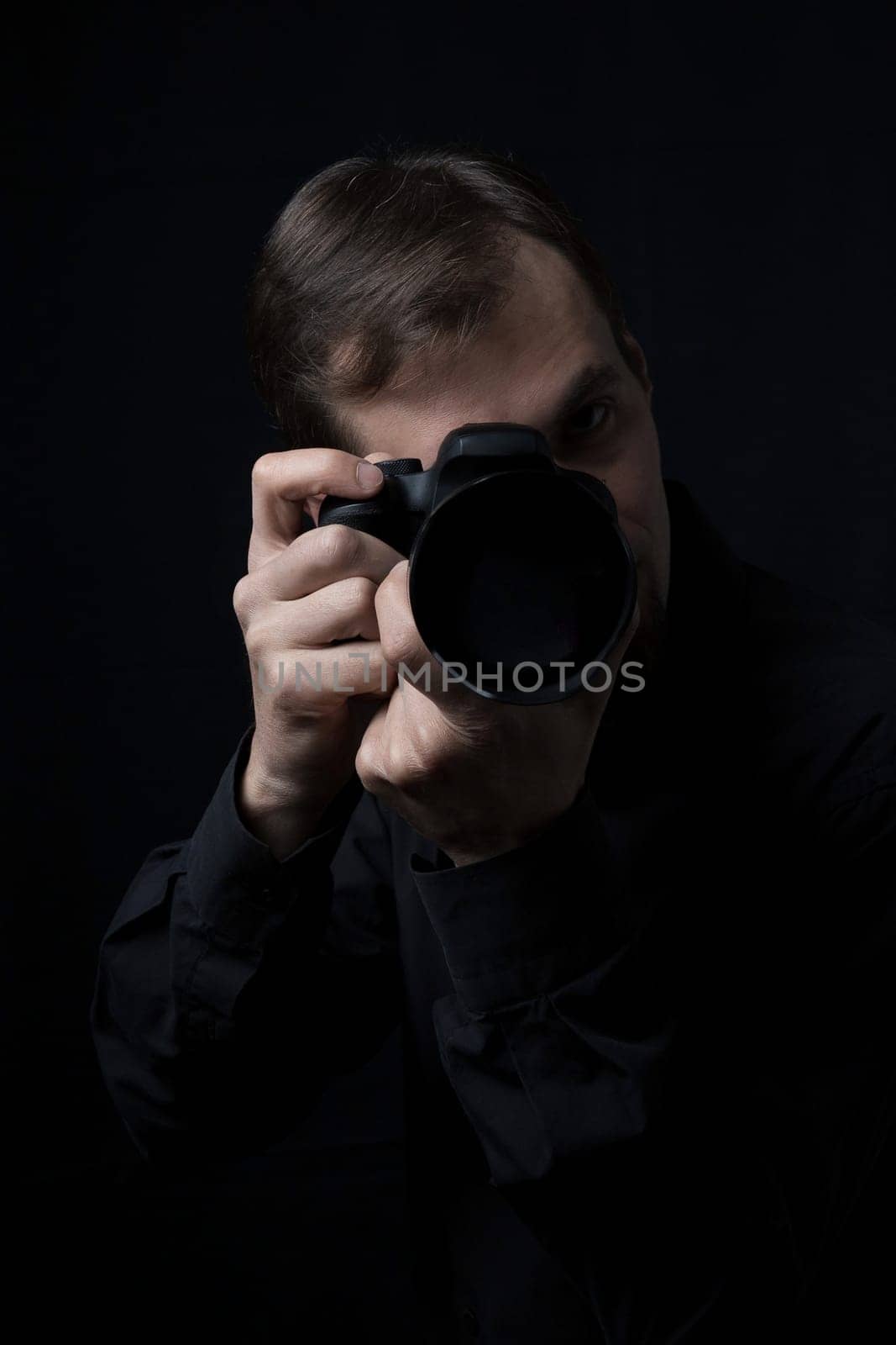 Low key portrait of a professional photographer man with a camera in the dark, look at camera, copy space.