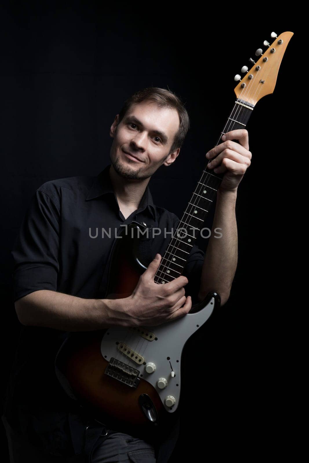 A man with an electric guitar looks at the camera.