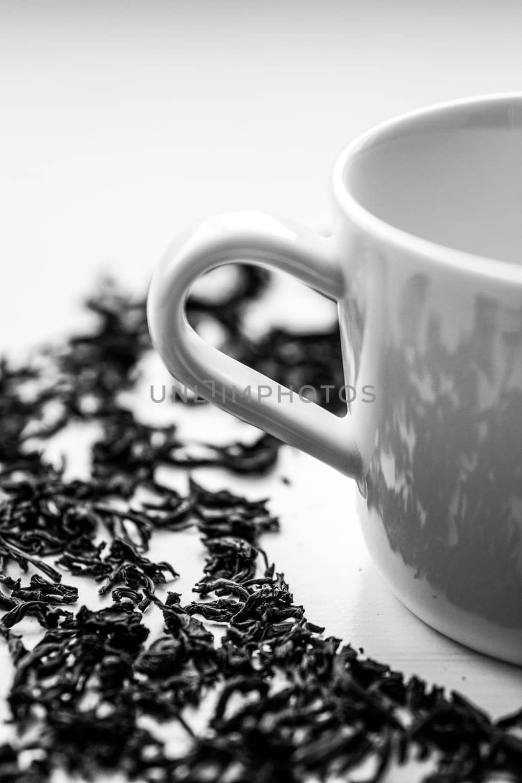 a close-up shot of a white cup on a white saucer and scattered black tea on the table next to the saucer by bySergPo