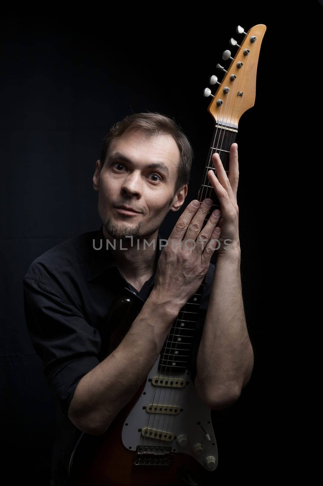 Expressive portrait of a caucasian man with an electric guitar on a dark background.
