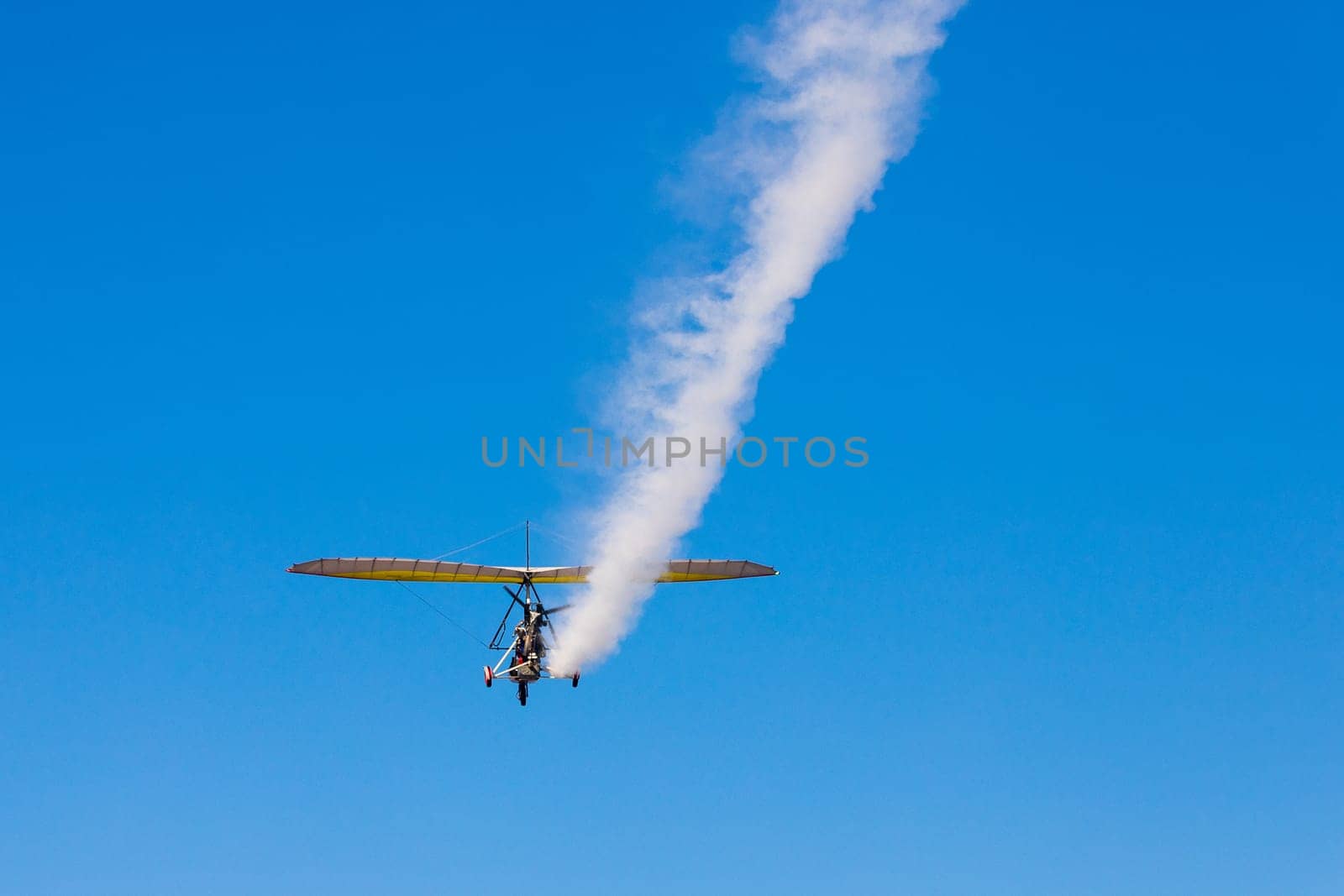 A paraglider with a cradle on wheels leaves a white trail in the blue sky.