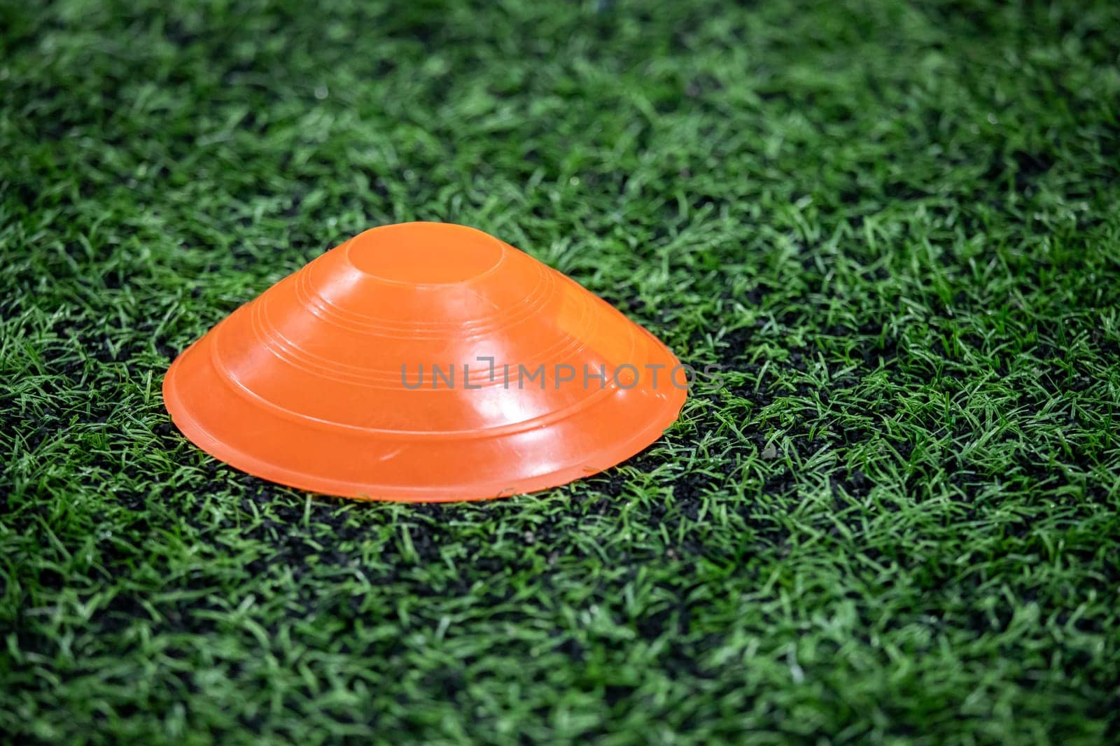 a pyramidal orange football cone on a green artificial turf. space for copying.