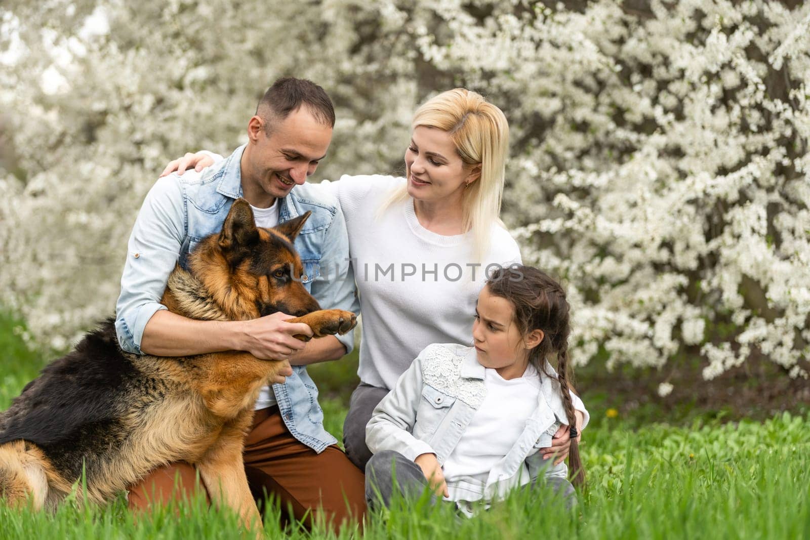 Outdoor portrait of happy young family playing in spring park under blooming tree, lovely family having fun in sunny garden.