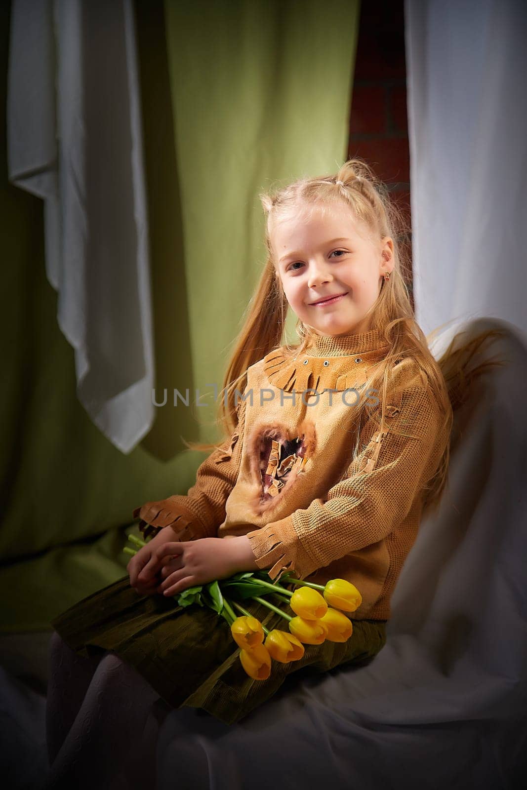 Portrait of a little blonde girl with bouquet of spring yellow flowers on a light background. Child in green dress holding a bouquet of tulips in hands. Spring concept