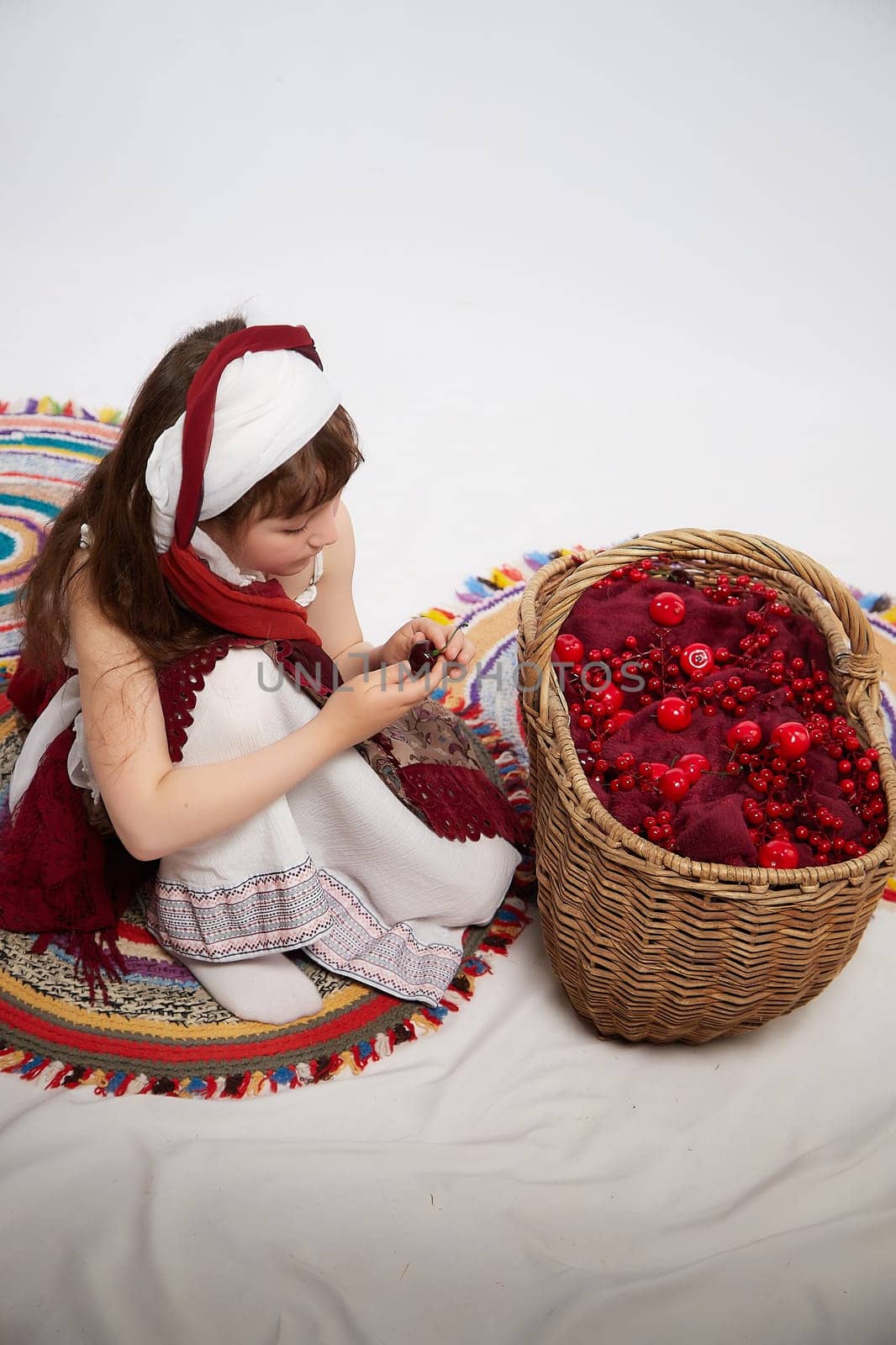 Portrait of Little girl in a stylized Tatar national costume with a large basket of red berries on a white background in the studio. Photo shoot of funny young teenager who is not a professional model