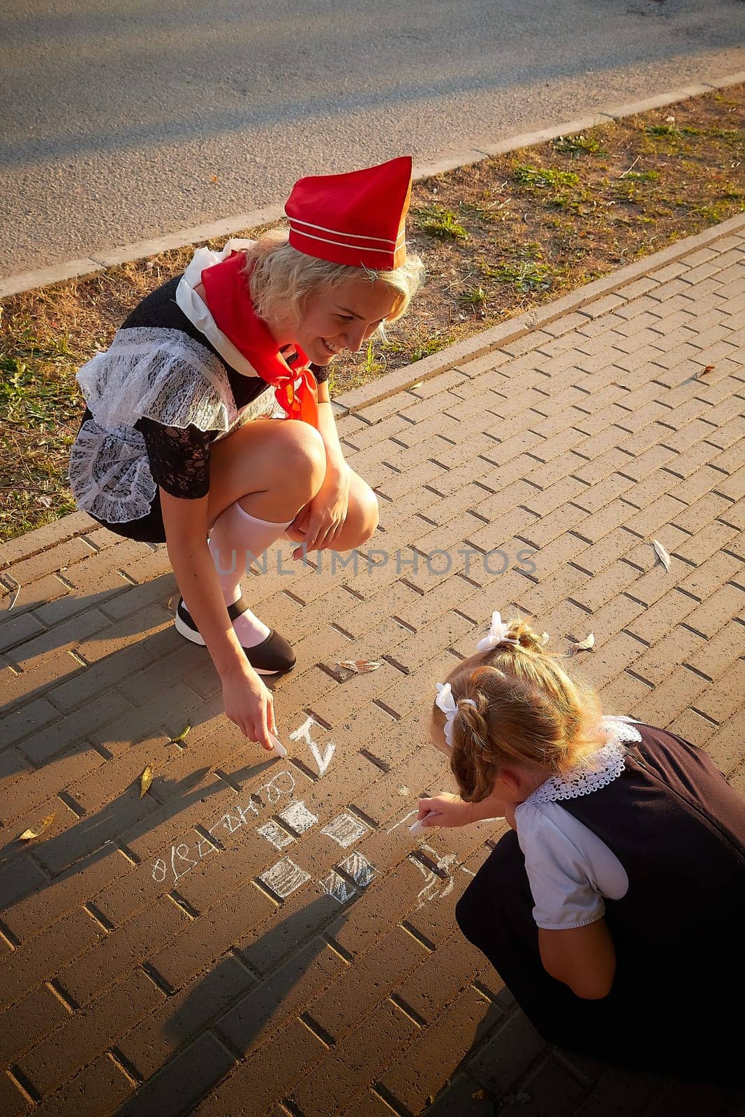 Young and adult schoolgirl on September 1 drawing by chalk on asphalt. Generation of schoolchildren of USSR and Russia. Female pioneer in red tie and October girl in modern uniform. Mom and daughter by keleny