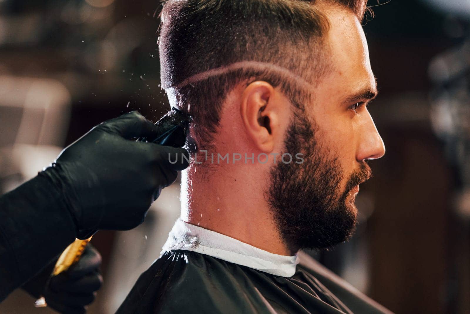 Young bearded man sitting and getting haircut in barber shop by Standret