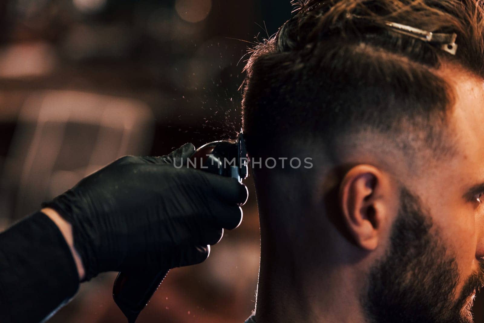 Close up view of young bearded man that sitting and getting haircut in barber shop by Standret