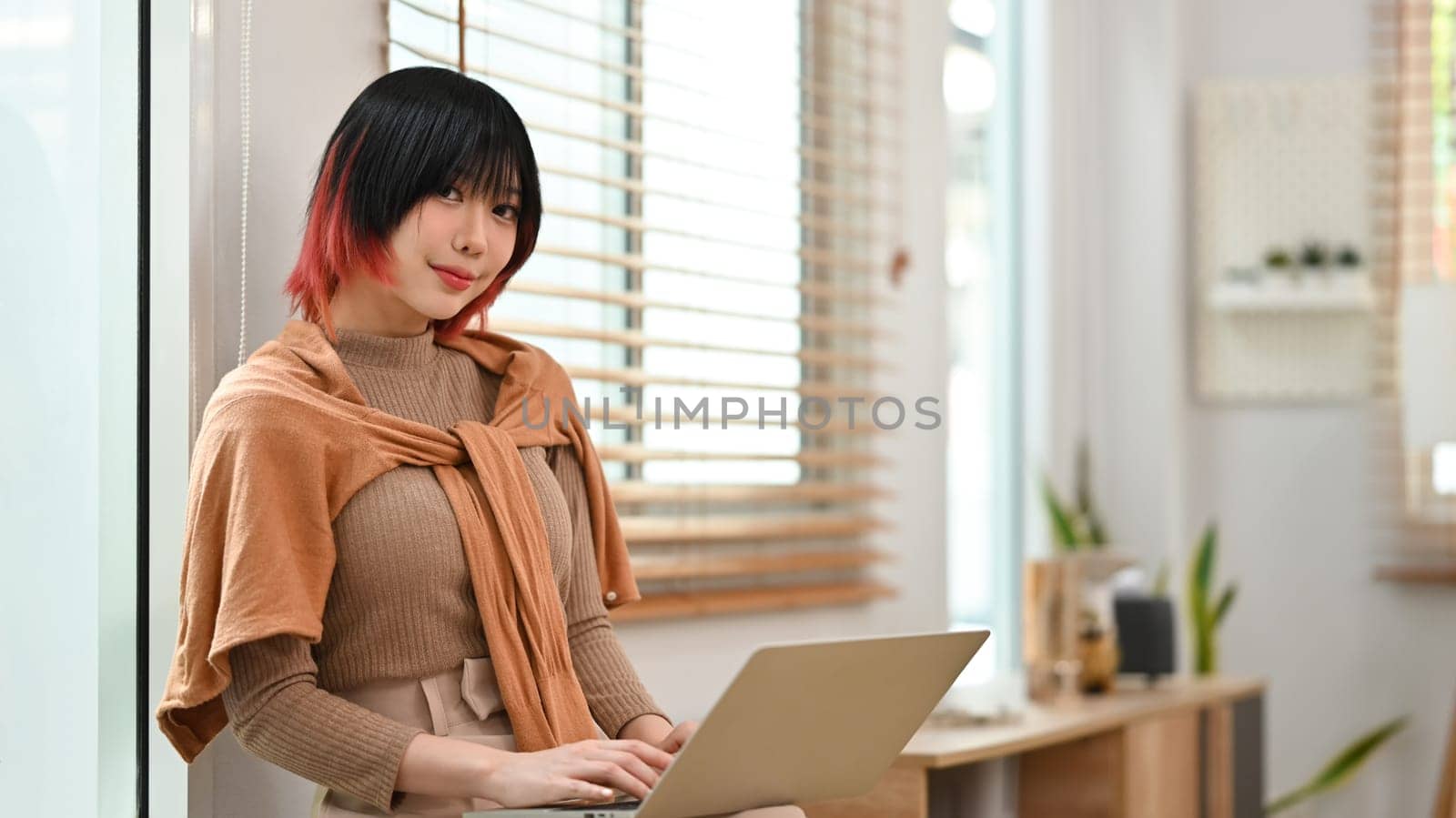 Portrait of pretty asian woman in stylish outfit using laptop at home office. Freelance, creative occupation, e-learning concept.