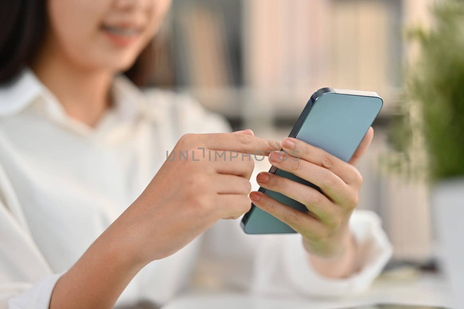 Selective focus on hands. Smiling young woman typing massage on her mobile phone while sitting at workplace.