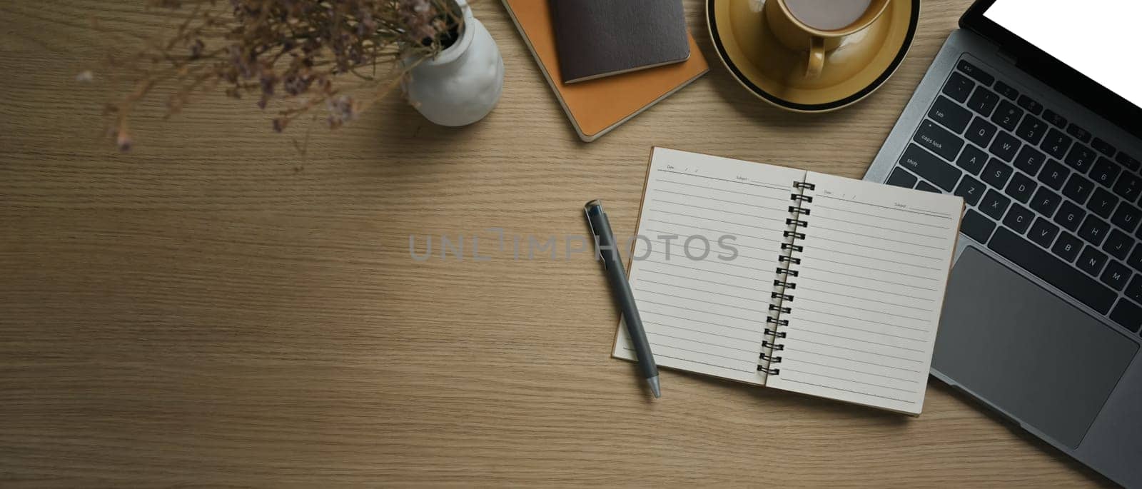 Top view of open notebook, laptop, cup of coffee and notepad on wooden working desk by prathanchorruangsak