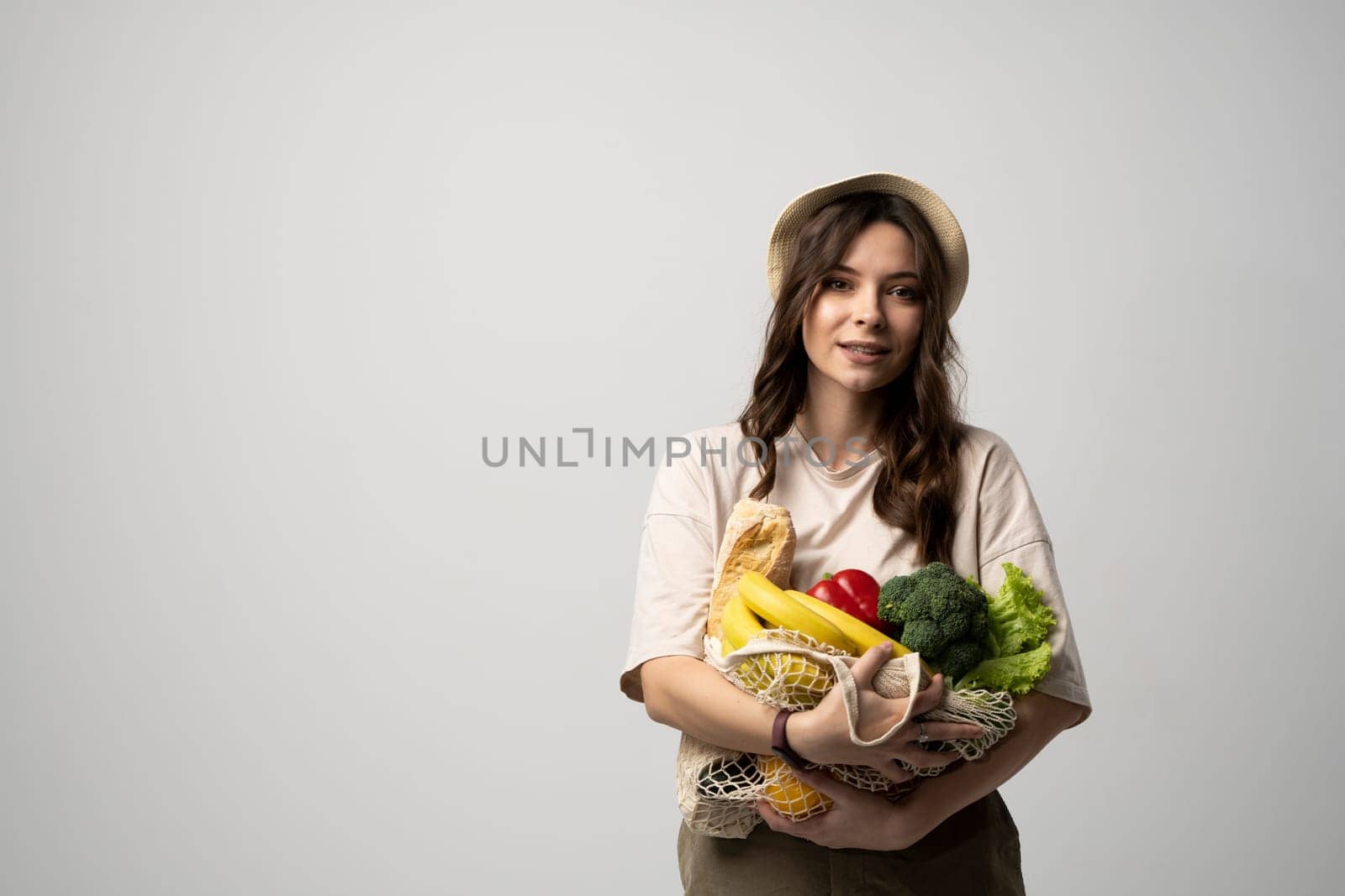 Zero waste concept. Young brunette woman holding reusable cotton shopping mesh bag with organic groceries from a market. Concept of no plastic. Zero waste, plastic free. Sustainable lifestyle