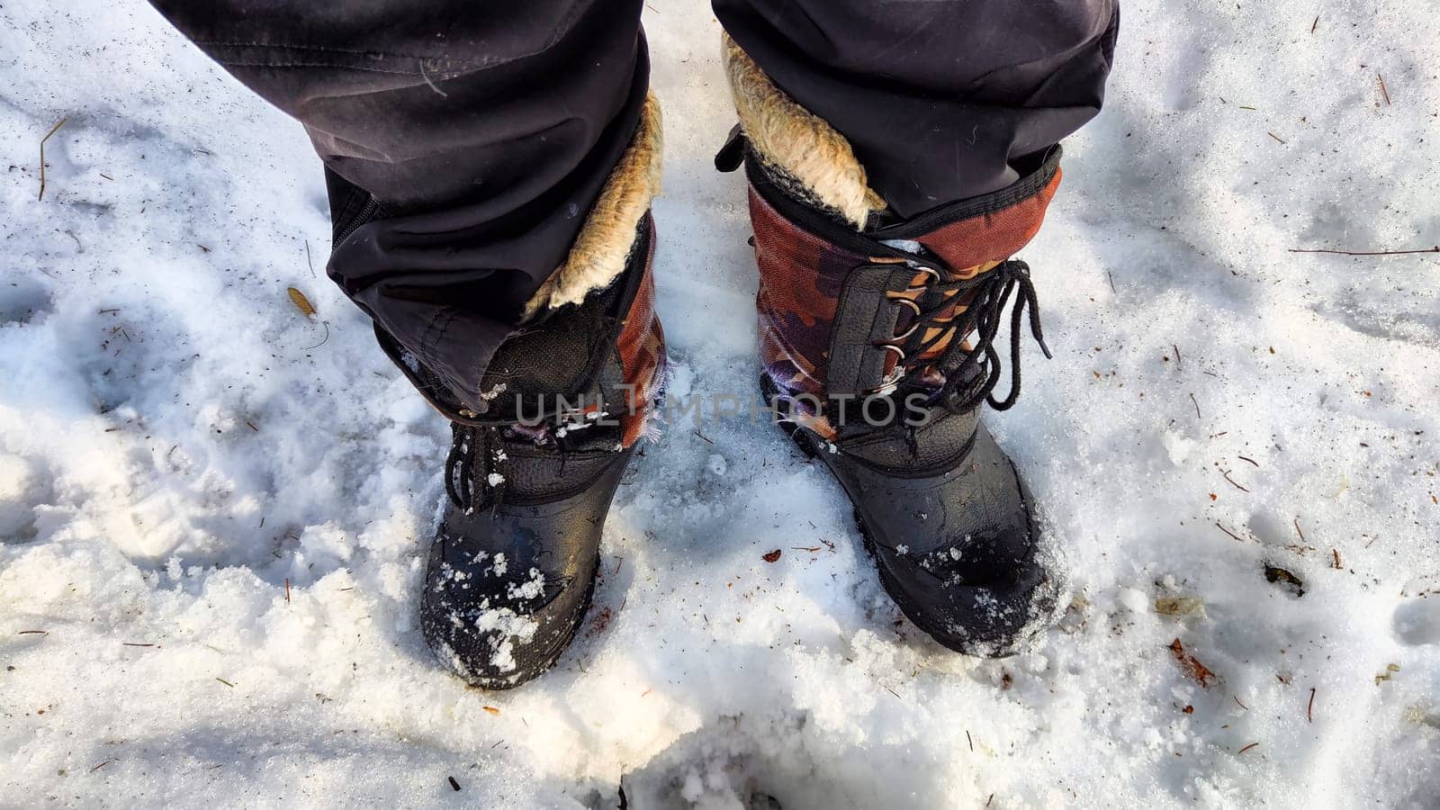 Feet of Hunter or fisherman in big warm boots on a winter day on snow. Top view. A fisherman on the ice of river, lake, reservoir on a spring day with melting ice. Dangerous fishing