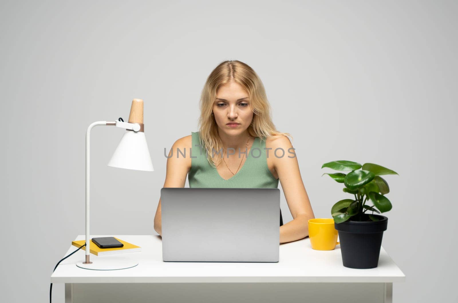 Smiling business woman working with a laptop isolated on a grey background. Portrait of a pretty young woman studying while sitting at the table with grey laptop computer, notebook.