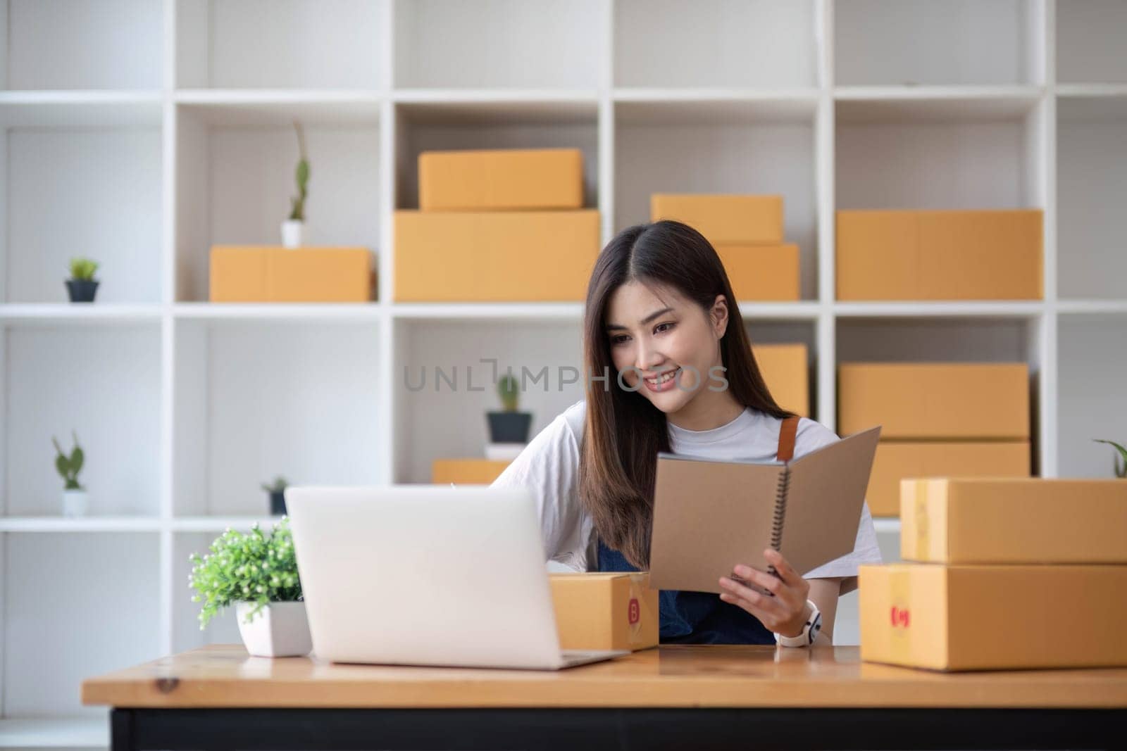Happy young Asian woman entrepreneur, Take note after check order and Smile for sale success of online shopping store, Concept of the merchant, small business, online business, and eCommerce...