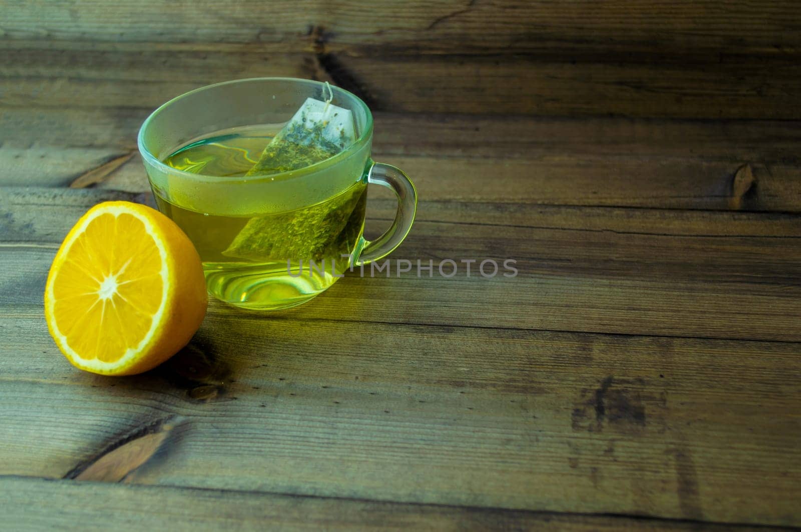 Green tea with lemon. Green tea in a glass mug and lemon on a wooden table.