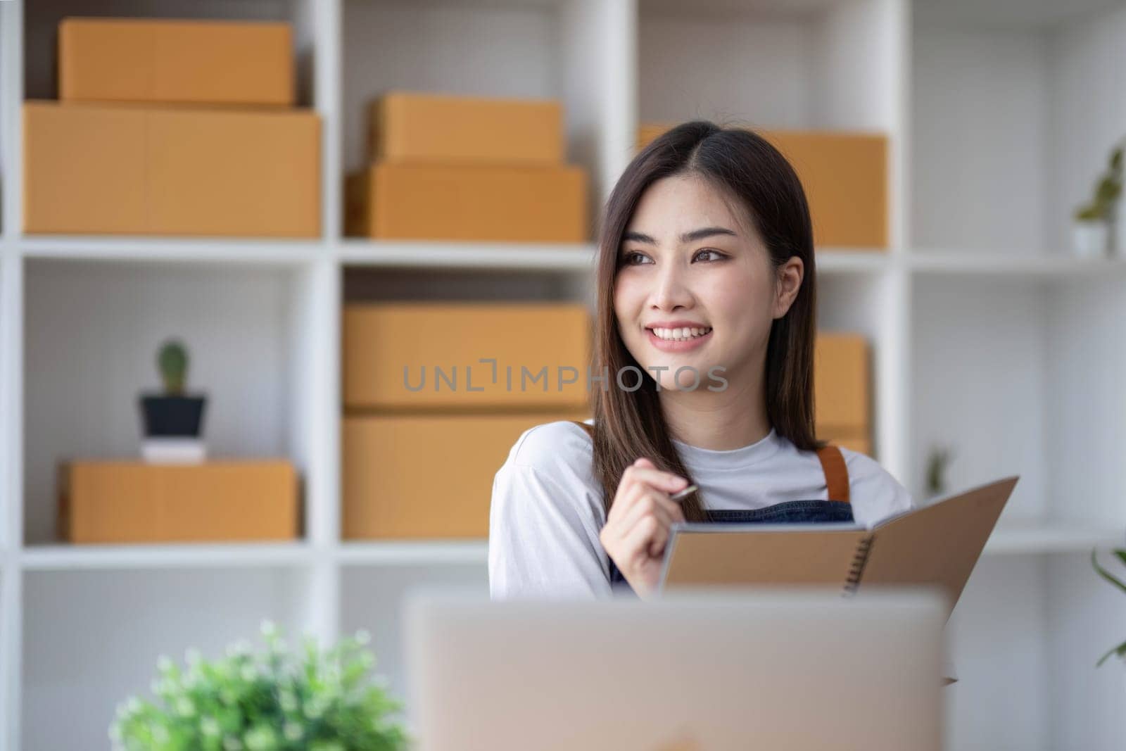 Happy young Asian woman entrepreneur, Take note after check order and Smile for sale success of online shopping store, Concept of the merchant, small business, online business, and eCommerce...