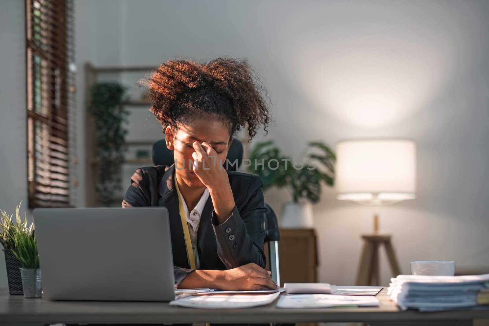 Young African American woman with afro hairstyle looks annoyed and stressed, sitting at the desk, using a laptop, thinking and looking at the camera, feeling tired and bored with depression problems..