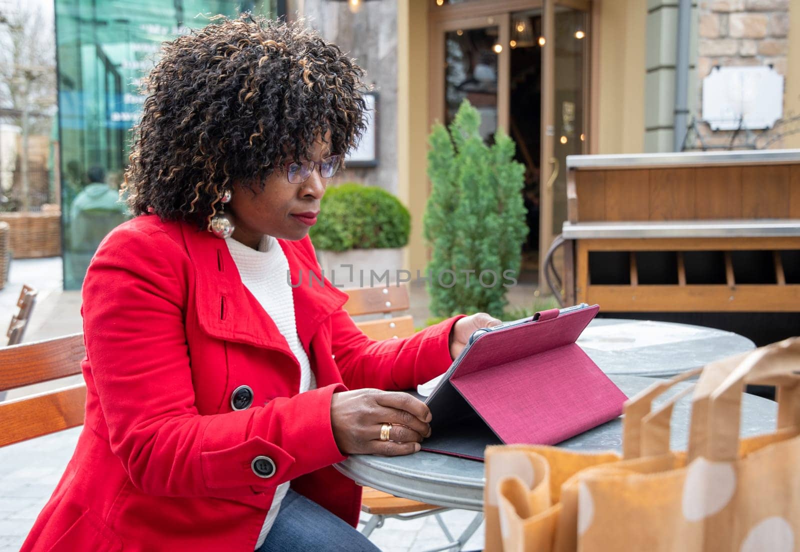 a young african american woman in a red coat sits at a table in a cafe and checking bill after shopping using a tablet, financial problems crisis, proper planning of expenses, High quality photo