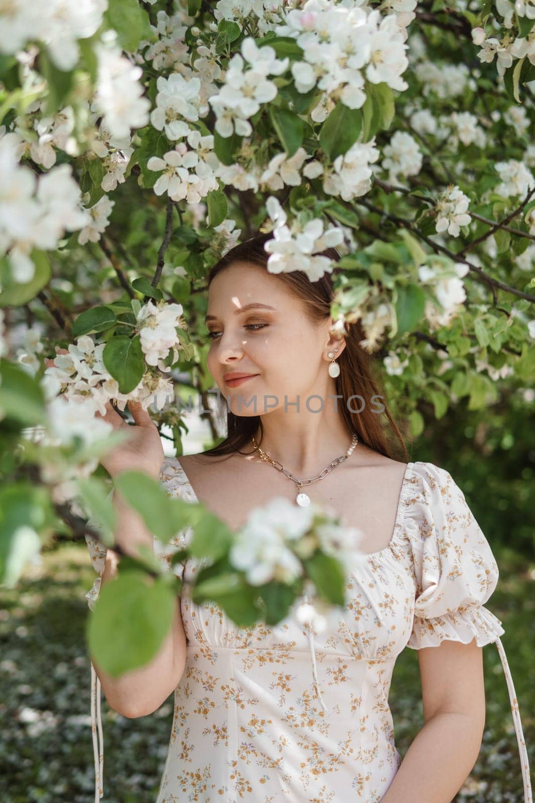 An attractive long-haired woman walks in the spring in the park of blooming apple trees. Spring portrait of a woman